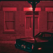 Red filtered picture of a car in front of building.